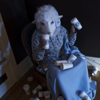 Person with the head of a sheep in a chair, coffee cups every where